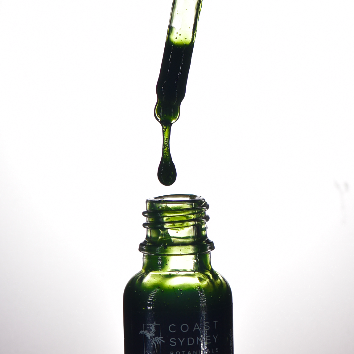 Close-up capturing the moment a serum droplet falls into the 'Simply A+' face serum bottle as a dropper hovers above the open bottle, releasing a luxurious green serum.