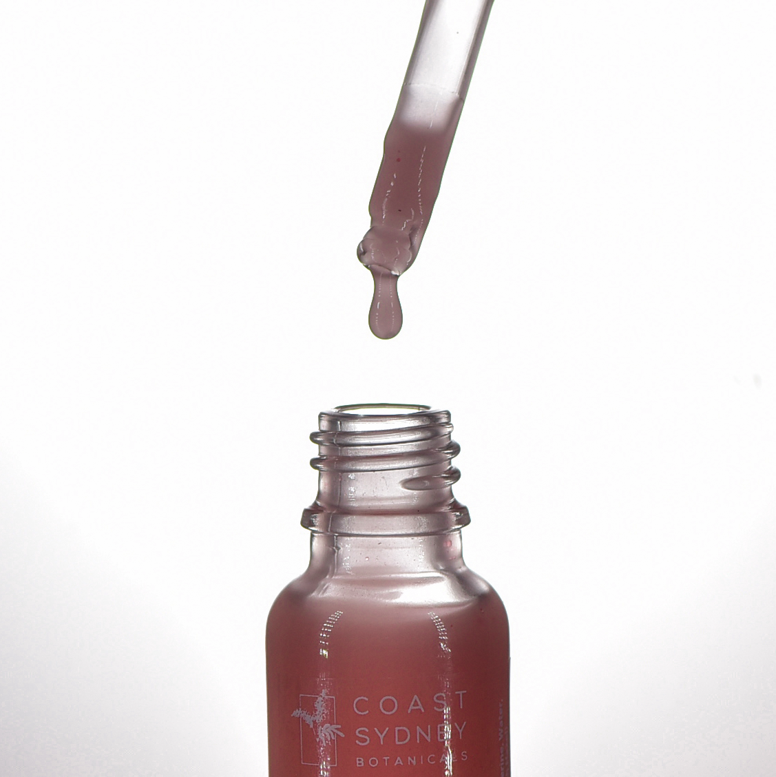 Close-up capturing the moment a serum droplet falls into the 'Simply Detox' face serum bottle as a dropper hovers above the open bottle, releasing a luxurious pink serum.
